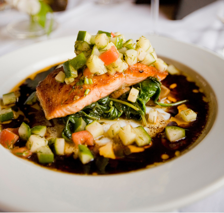 a salmon fillet on a bed of veggies and sauce