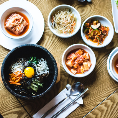 Korean food presented in different sized bowls. There are four white bowls and one black claypot bowl.