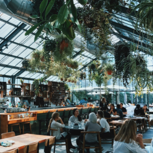 some people sitting at a restaurant filled with plants that has a glass ceiling 